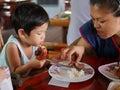 Little Asian baby girl being taught by her mother how to eat grilled pork slices and sticky rice by hands