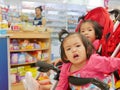 Little Asian baby girl front getting bored waiting for a long time in a baby stroller for her mother buying drugs a pharmacy