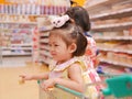 Little Asian baby girl having fun standing in a shopping cart with her sister while her mother does a shopping Royalty Free Stock Photo