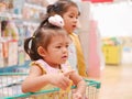 Little Asian baby girl having fun standing in a shopping cart with her sister seeing many products for sale Royalty Free Stock Photo