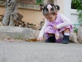 Little Asian baby girl reaching her hand out to touch something tiny on the surface of a street Royalty Free Stock Photo