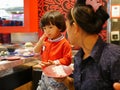 Little Asian baby girl tasting raw ingredients, for hotpot cooking, serving on a moving conveyor belt