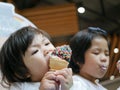 Little Asian baby girl, 2 years old, eating / biting ice cream cone, together with her older sister Royalty Free Stock Photo