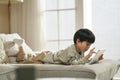 little asian boy lying on front on couch playing computer game using digital tablet Royalty Free Stock Photo