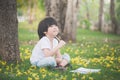 Little Asian boy sitting under the tree and drawing in notebook