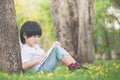 Little Asian boy sitting under the tree and drawing in notebook