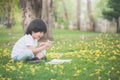 Little Asian boy sitting under the tree and drawing in notebook