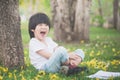 Little Asian boy sitting under the tree and drawing in notebook