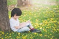 Little Asian boy sitting under the tree and drawing in notebook