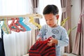 Little Asian boy using hanger hang up a clothes on wood rack