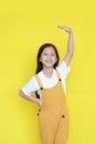 Little asian child girl measures the growth on yellow background. Kid estimate her height by hand with looking camera Royalty Free Stock Photo