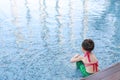 Little Asian child girl in a mermaid suit has fun sitting poolside. Rear view