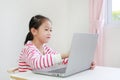 Little asian child girl sitting at desk and using laptop computer stay at home Royalty Free Stock Photo