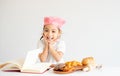 Little Asian girl action as cute and smile in front of notebook and bread on table with white background