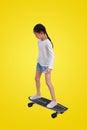 Little Asian girl child skating on a skateboard isolated on yellow background. Kid riding on skateboard with Clipping path Royalty Free Stock Photo