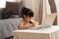 Little Asian girl child study online learn on laptop at home smile and happiness.Cute girl drawing and handwriting in notebook to