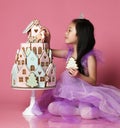 Little asian girl in crown and purple dress with ginger cookie cake birthday celebration on pink