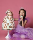 Little asian girl in crown and purple dress with ginger cookie cake for birthday party celebration