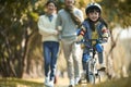 Little asian girl riding bike in city park with parents in background Royalty Free Stock Photo