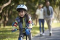 Little asian girl riding bike in city park with parents in background Royalty Free Stock Photo