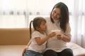 Little asian girl and her pregnant mom drinking milk sitting on sofa near the window at home. Motherhood and care, healthy eating Royalty Free Stock Photo