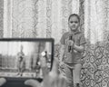 Little Asian girl holding microphone at home concert. Hands holding tablet for taking video Royalty Free Stock Photo