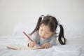 Little Asian girl lying on bed and writing alphabet on notebook