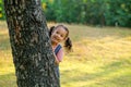 Little Asian girl play peekaboo by hiding back of tree and smile, she play in green garden with morning light Royalty Free Stock Photo