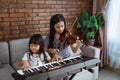 Little asian girl plays a musical instrument keyboard with her sister playing the violin together Royalty Free Stock Photo