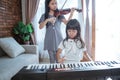 Little asian girl plays a musical instrument keyboard with her sister playing the violin together Royalty Free Stock Photo