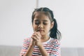 Little asian girl praying while sitting on sofa in living room at home Royalty Free Stock Photo