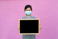 Little asian girl in a protective medical mask holding black board isolated on pink background. Royalty Free Stock Photo