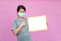 Little asian girl in a protective medical mask holding white board isolated on pink background. Royalty Free Stock Photo