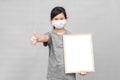 Little asian girl in a protective medical mask holding whiteboard isolated on gray background.