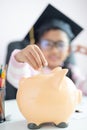 Little Asian girl putting the coin into piggy bank and smile with happiness for money saving to wealthness in the future of Royalty Free Stock Photo