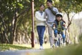 Little asian girl riding bike in city park with parents in background Royalty Free Stock Photo