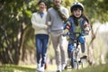 Little asian girl riding bike in city park with parents in background Royalty Free Stock Photo