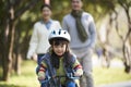 Little asian girl riding bike in city park with parents in background Royalty Free Stock Photo