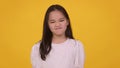 Little asian girl shaking her head in denial and frowing her face, orange studio background, slow motion