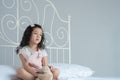 Little Asian girl sitting on bed with a teddy bear thinking and looking out of her bedroom Royalty Free Stock Photo