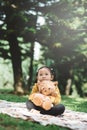 Little asian girl sitting in park while hugging her teddy bear with sad face. Royalty Free Stock Photo