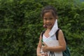 Little asian girl wearing face mask with green back pack holding stationery in green nature park background. Back to school Royalty Free Stock Photo