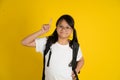 Little Asian girl wearing glasses and carrying a school bag with her finger pointing up, on a yellow background Royalty Free Stock Photo