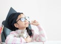 Little Asian girl wearing graduate hat hugging clear glass jar piggy bank and smile with happiness for money saving to wealthness Royalty Free Stock Photo