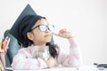 Little Asian girl wearing graduate hat hugging clear glass jar piggy bank and smile with happiness for money saving to wealthness Royalty Free Stock Photo