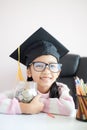 Little Asian girl wearing graduate hat hugging clear glass jar piggy bank and smile with happiness for money saving to wealthness Royalty Free Stock Photo