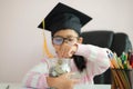 Little Asian girl wearing graduate hat putting the coin into clear glass jar piggy bank and smile with happiness for money saving Royalty Free Stock Photo