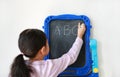 Little Asian girl writing ABC on blank black board on white background. Education concept. Rear view Royalty Free Stock Photo