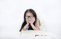 Little Asian kid girl wearing glasses reading hardcover book lying on bed against white background Royalty Free Stock Photo