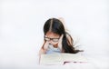 Little Asian kid girl wearing glasses reading hardcover book lying on bed against white background Royalty Free Stock Photo
